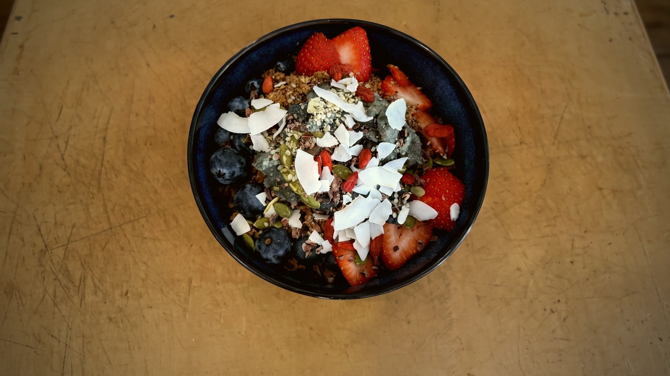An açaí bowl in a dark navy ceramic bowl on a warm plywood table at Golden Sol