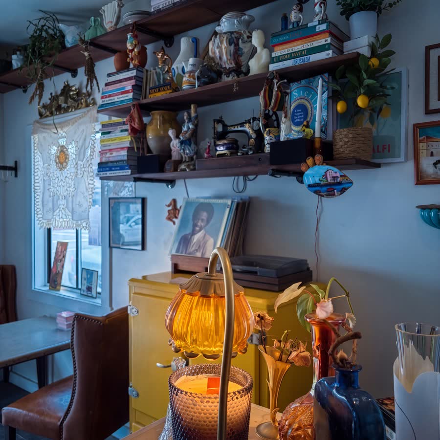A corner of Golden Sol — shelves of books, plants and ceramics above a record player, a yellow cabinet and an amber lamp